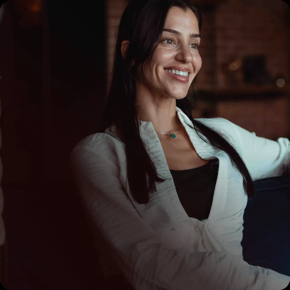 A smiling Rewind Aesthetics client relaxing on a sofa