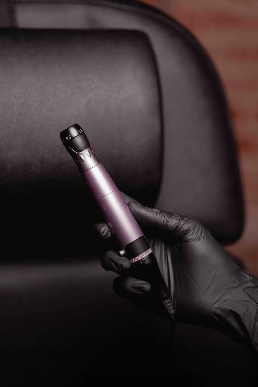 Gloved hand holding a microneedling pen