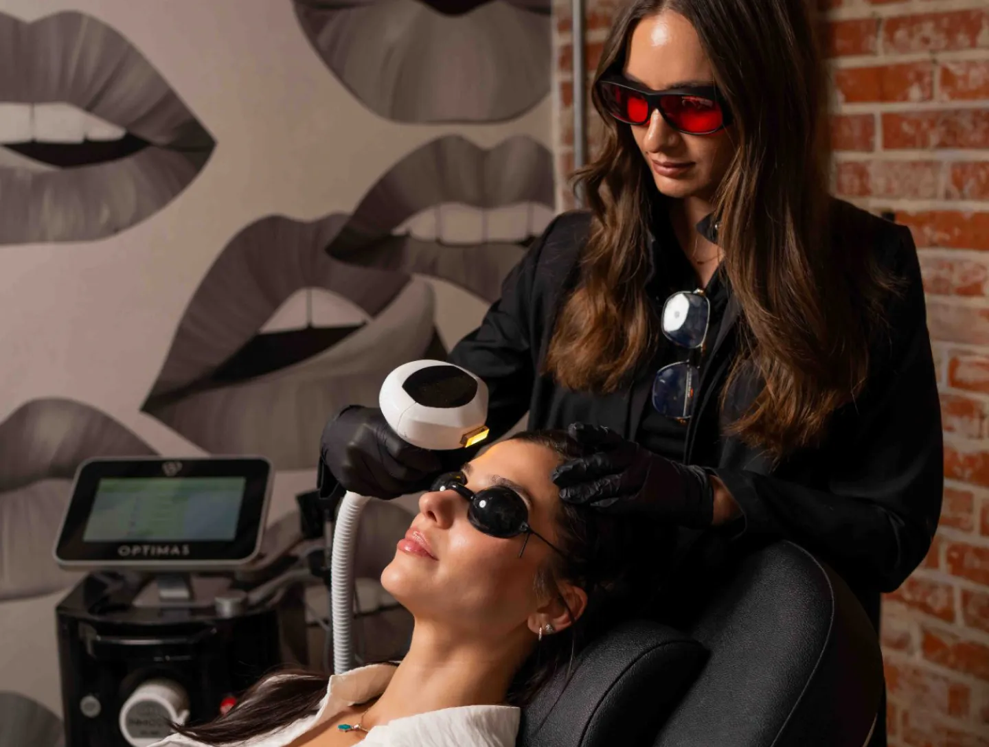 A provider in red safety glasses performing an IPL photofacial on a client