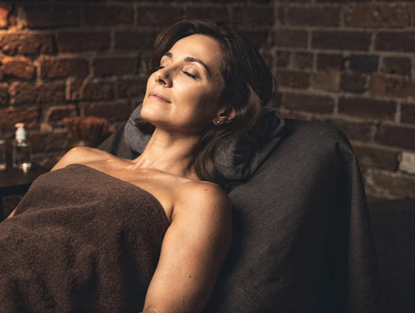 A client relaxing under a towel during a facial in a brick-walled treatment room