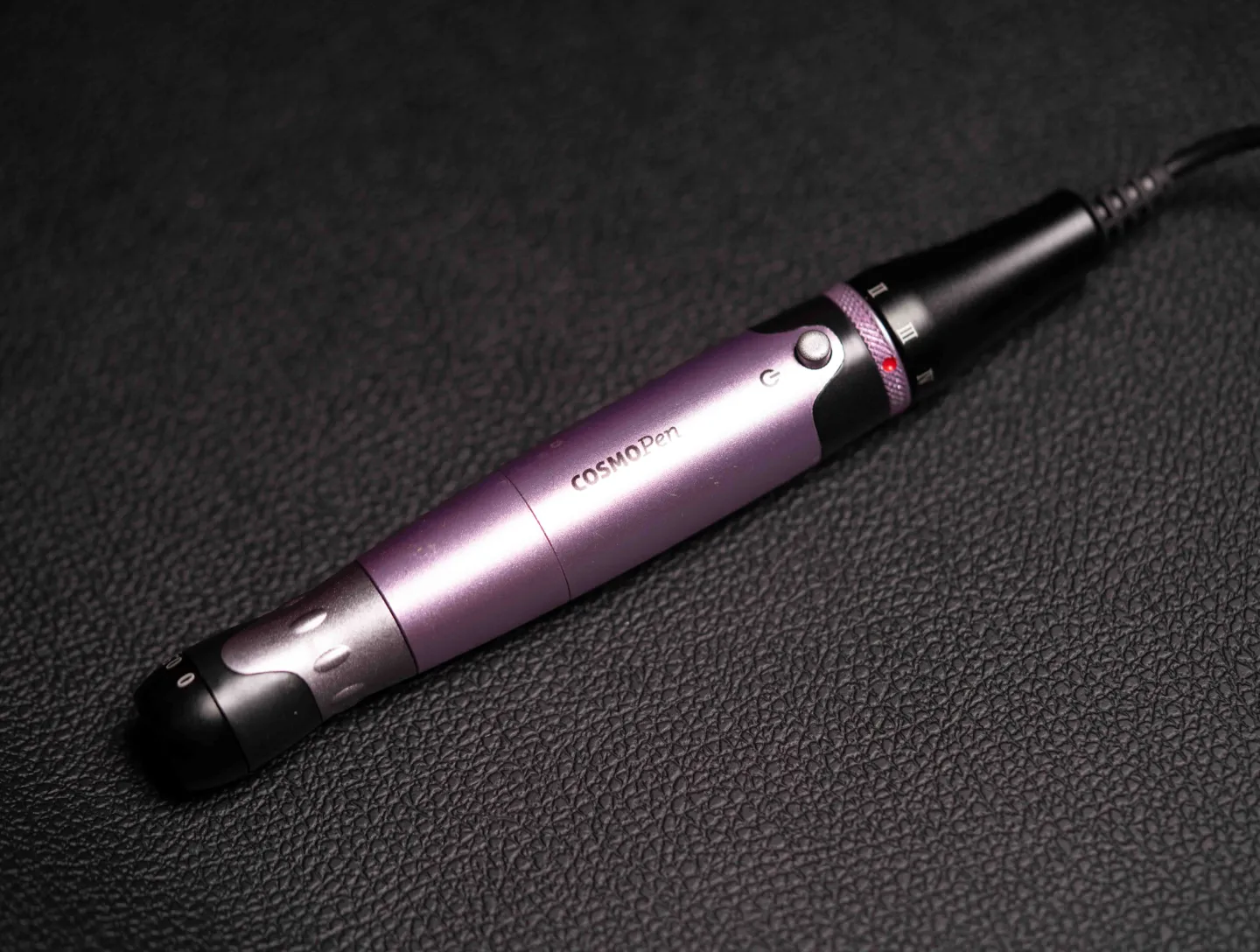 A microneedling pen resting on a dark leather surface