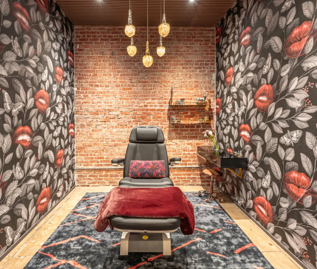 Private treatment room at Rewind Aesthetics with floral lips wallpaper and a red-draped treatment chair