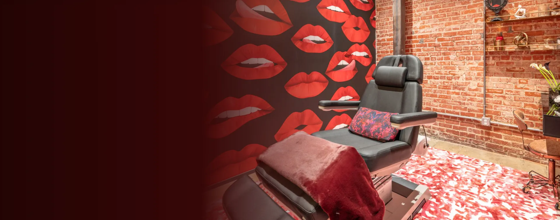 A Rewind Aesthetics treatment room with a red lips mural, brick walls and a black treatment chair