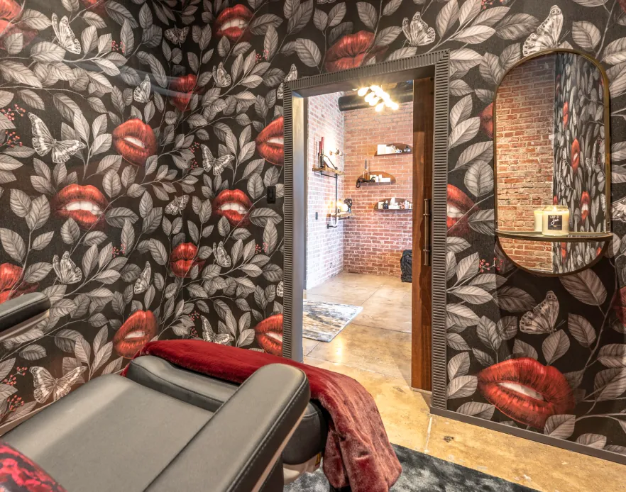 Treatment room with leaf-and-lips wallpaper and a red-draped chair