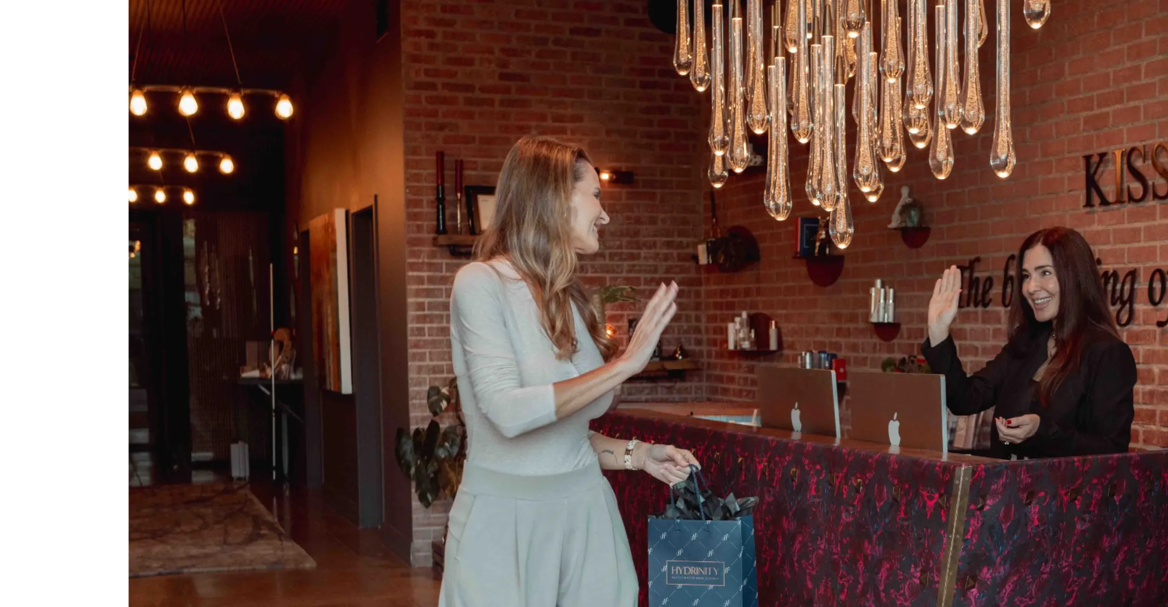 A Rewind Aesthetics team member greeting a client at the front desk under the crystal light installation